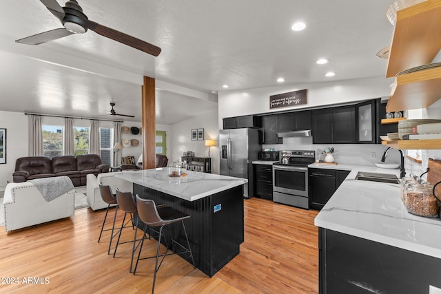 kitchen with light hardwood / wood-style floors, a center island, sink, a kitchen bar, and appliances with stainless steel finishes