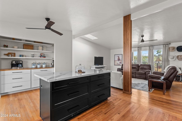 kitchen with light wood-type flooring, white cabinets, vaulted ceiling, a kitchen island, and ceiling fan