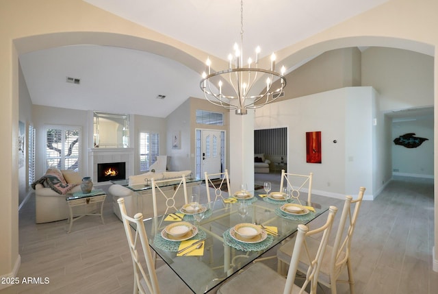 dining space with lofted ceiling, a fireplace, a notable chandelier, and light wood-type flooring