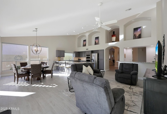 living room with a towering ceiling, ceiling fan with notable chandelier, and light hardwood / wood-style flooring