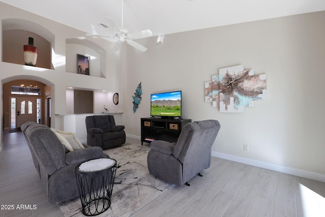 living room with ceiling fan, a high ceiling, and light wood-type flooring