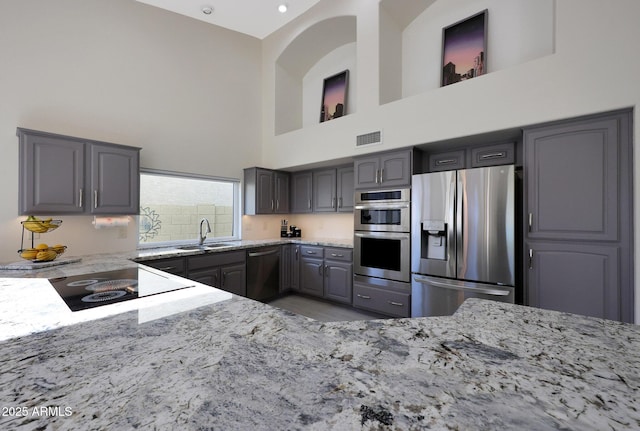 kitchen with gray cabinetry, sink, a high ceiling, light stone counters, and appliances with stainless steel finishes