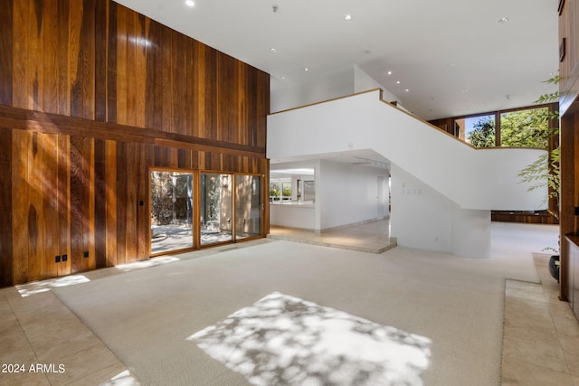 unfurnished living room with wooden walls, plenty of natural light, light carpet, and a high ceiling