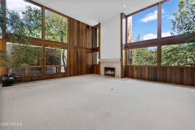 unfurnished living room featuring carpet flooring, wooden walls, and a high ceiling