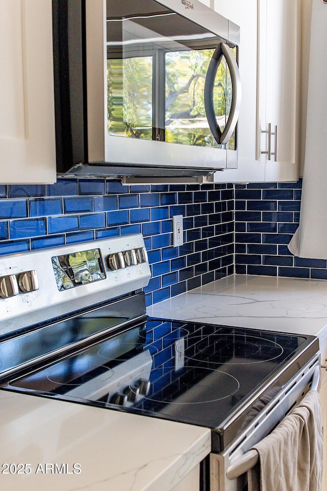 room details featuring stainless steel appliances, white cabinetry, light stone counters, and decorative backsplash