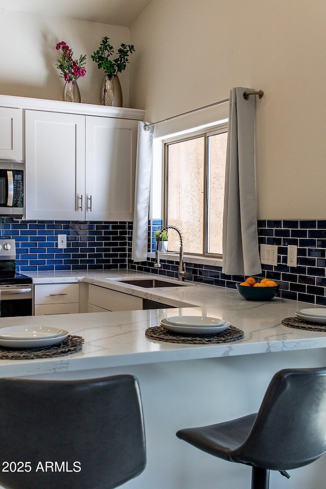 kitchen with tasteful backsplash, appliances with stainless steel finishes, sink, and white cabinets