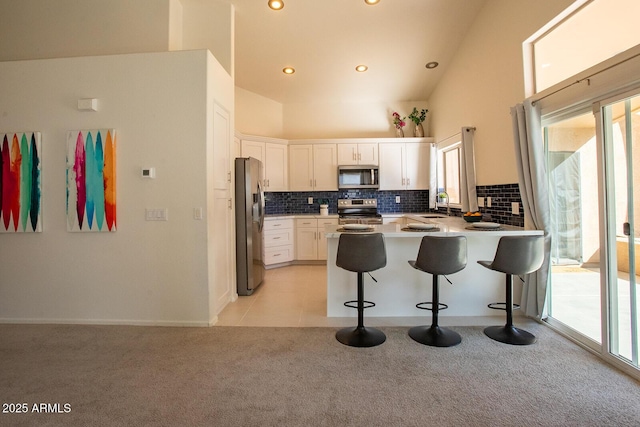 kitchen featuring a kitchen breakfast bar, stainless steel appliances, white cabinets, light carpet, and kitchen peninsula