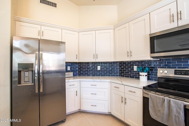 kitchen featuring light tile patterned floors, white cabinetry, backsplash, stainless steel appliances, and light stone counters