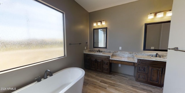 bathroom with double vanity, a freestanding tub, a sink, and wood finished floors