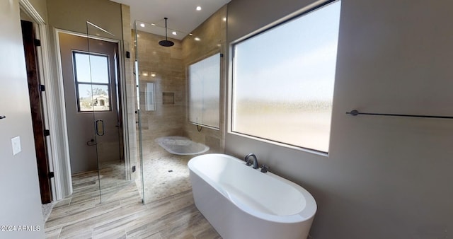 bathroom with a shower stall, a freestanding bath, and wood finished floors