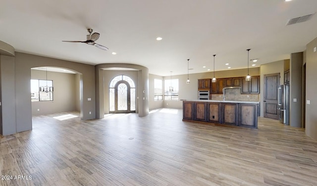 kitchen featuring backsplash, ceiling fan with notable chandelier, a spacious island, hanging light fixtures, and light hardwood / wood-style flooring