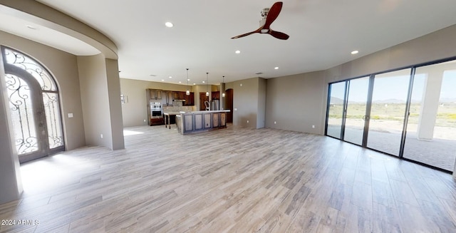 unfurnished living room with arched walkways, french doors, recessed lighting, ceiling fan, and light wood-type flooring