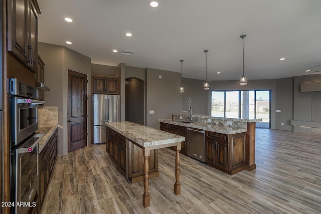 kitchen with stainless steel appliances, light stone counters, hanging light fixtures, and an island with sink