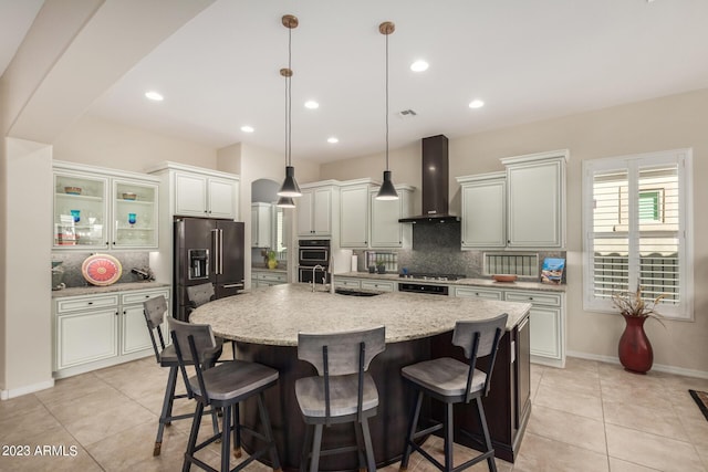 5771 W Cinder Brook Way, Florence, AZ 85132 - kitchen with wall chimney exhaust hood, high end black fridge, tasteful backsplash, light tile patterned floors, and a large island with sink