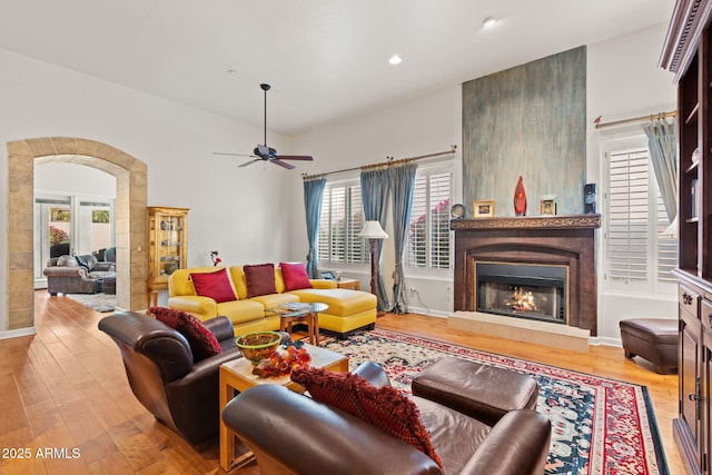 living room featuring ceiling fan, a large fireplace, and light hardwood / wood-style floors