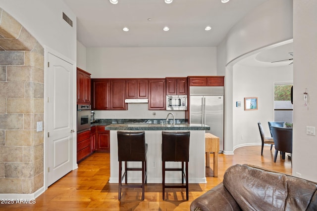 kitchen featuring sink, built in appliances, an island with sink, light hardwood / wood-style floors, and a kitchen bar