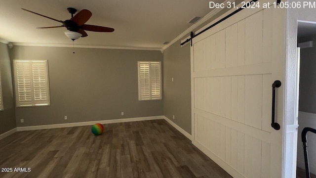 empty room featuring a barn door, baseboards, dark wood finished floors, ceiling fan, and crown molding