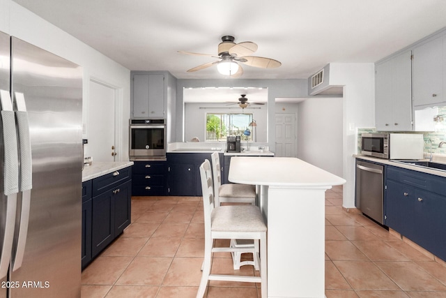 1308 N 66th St, Scottsdale, AZ 85257 - kitchen with appliances with stainless steel finishes, a ceiling fan, light countertops, light tile patterned floors, and a breakfast bar area