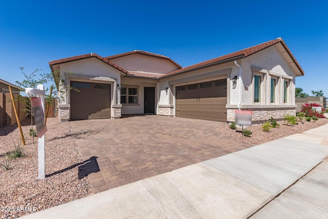 view of front of house featuring decorative driveway, stone siding, a tiled roof, and a garage
