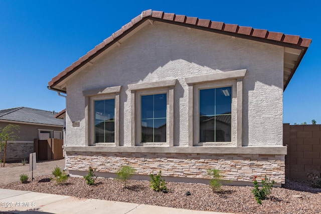 view of property exterior with stone siding, stucco siding, and fence