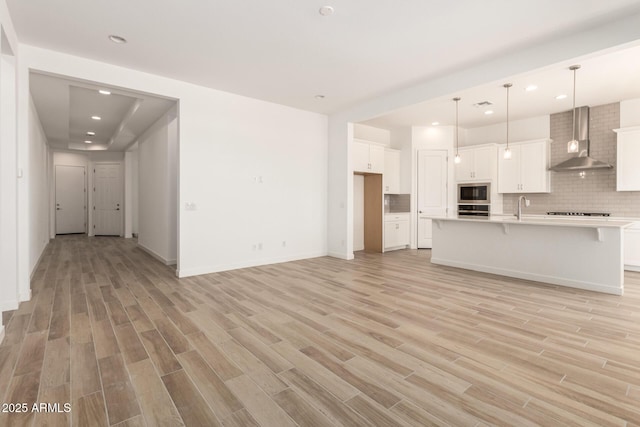 interior space with light wood finished floors, stainless steel appliances, wall chimney exhaust hood, backsplash, and open floor plan