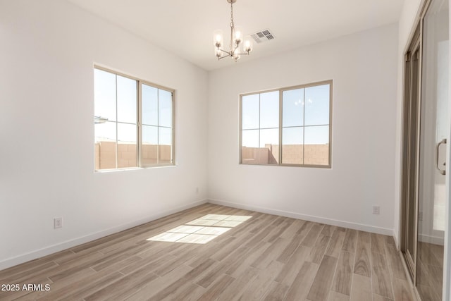 spare room featuring a notable chandelier, light wood finished floors, visible vents, and baseboards