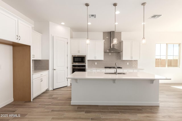 kitchen featuring built in microwave, light wood-type flooring, oven, wall chimney exhaust hood, and visible vents