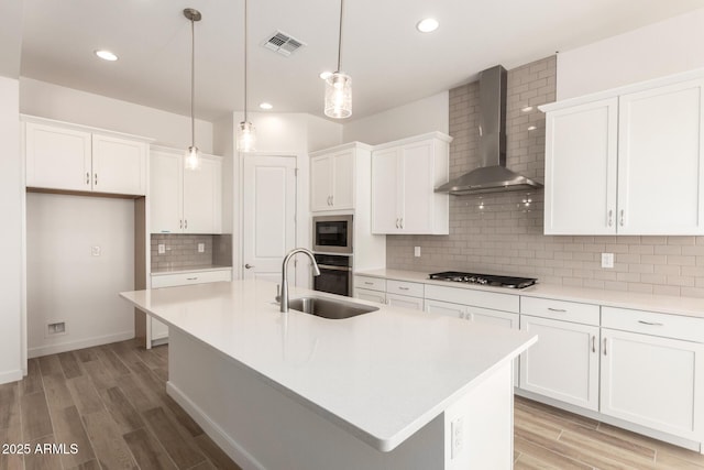 kitchen with wall chimney range hood, light wood-type flooring, a sink, white cabinetry, and visible vents