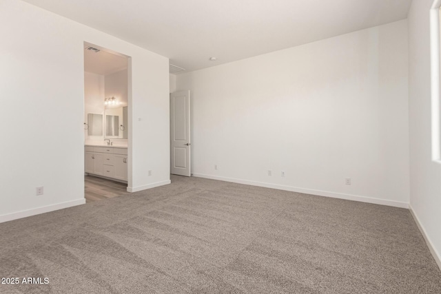 unfurnished bedroom featuring baseboards, light carpet, connected bathroom, and a sink