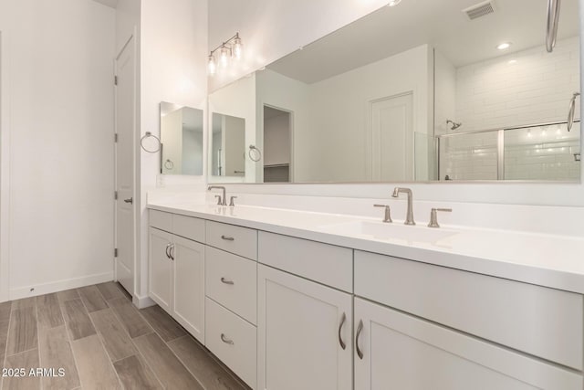 bathroom featuring a sink, tiled shower, double vanity, visible vents, and wood finished floors