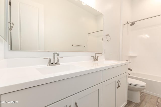 bathroom featuring toilet, double vanity, a sink, and wood finished floors