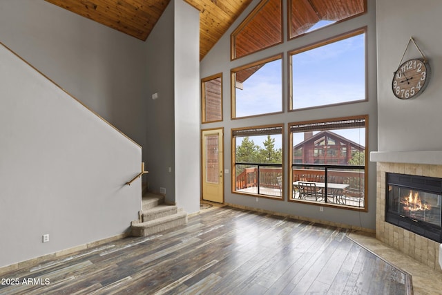 unfurnished living room with stairway, wood finished floors, high vaulted ceiling, a fireplace, and wood ceiling