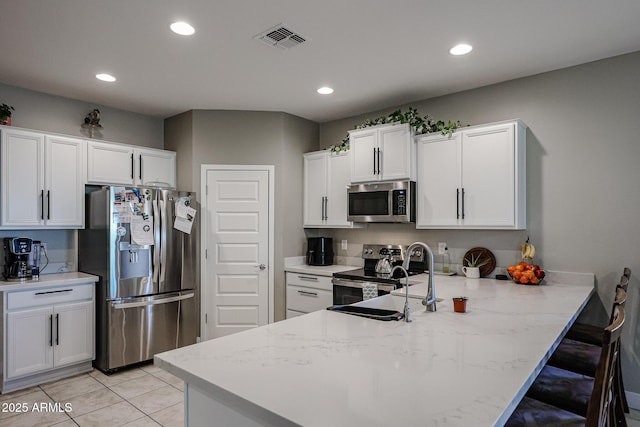 kitchen with sink, light tile patterned floors, white cabinetry, stainless steel appliances, and kitchen peninsula