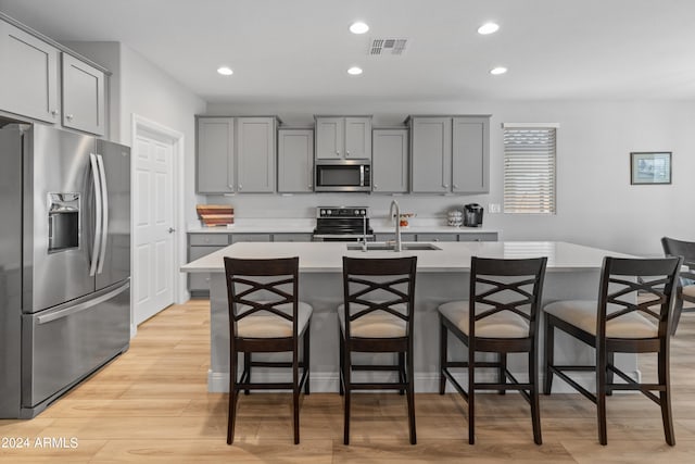 kitchen featuring a breakfast bar, a kitchen island with sink, sink, light hardwood / wood-style flooring, and appliances with stainless steel finishes