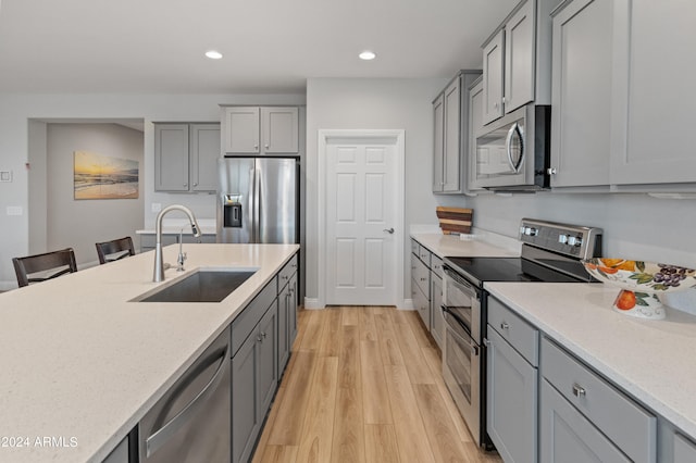 kitchen featuring sink, gray cabinets, appliances with stainless steel finishes, a kitchen breakfast bar, and light hardwood / wood-style floors