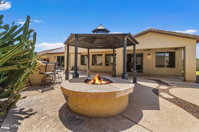 rear view of house with a gazebo, an outdoor fire pit, stucco siding, and a patio