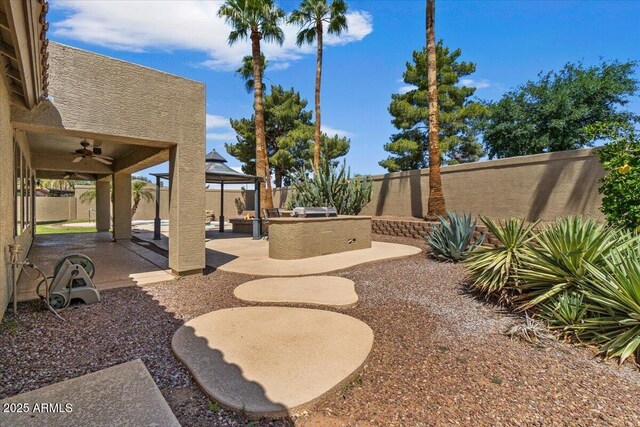 view of yard featuring a gazebo, an outdoor kitchen, a fenced backyard, a ceiling fan, and a patio