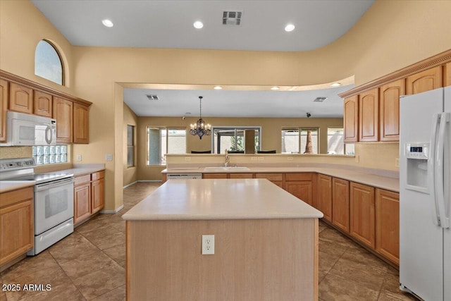 kitchen featuring visible vents, a peninsula, white appliances, a center island, and a sink