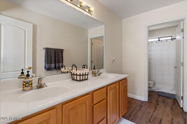 bathroom featuring double vanity, toilet, a sink, and wood finished floors
