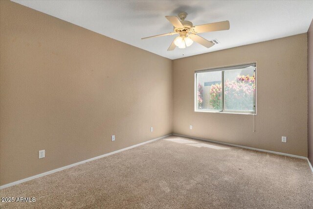 carpeted spare room featuring baseboards, a ceiling fan, and visible vents