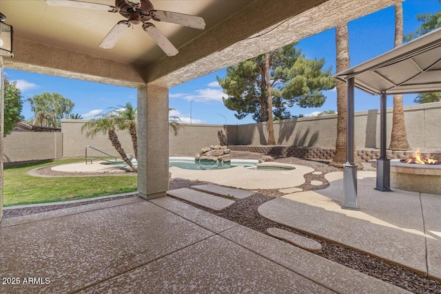 view of patio / terrace featuring a fenced backyard, ceiling fan, a fire pit, and an in ground hot tub