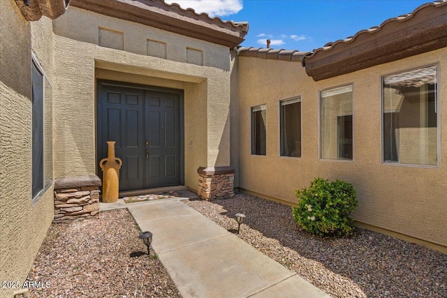 entrance to property with stucco siding, a tiled roof, and stone siding