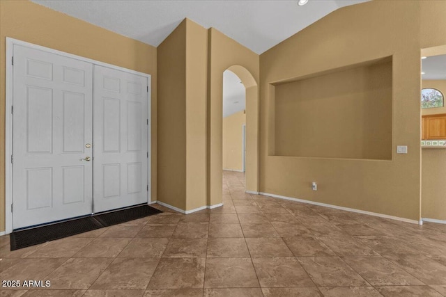 foyer with arched walkways, baseboards, and lofted ceiling