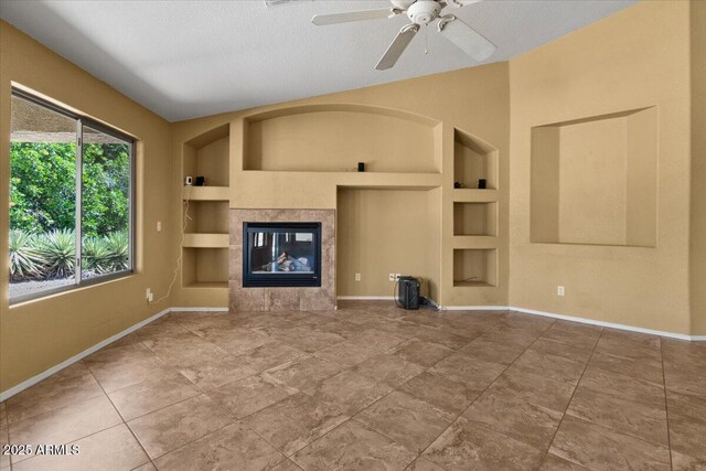 unfurnished living room with baseboards, ceiling fan, a textured ceiling, built in shelves, and a tile fireplace