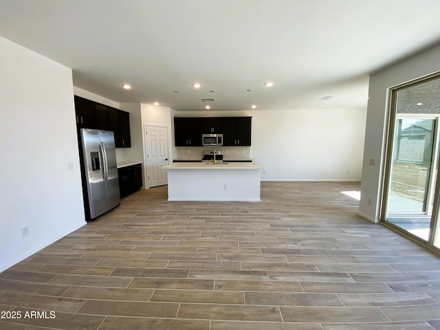 kitchen featuring open floor plan, light countertops, appliances with stainless steel finishes, wood finish floors, and backsplash