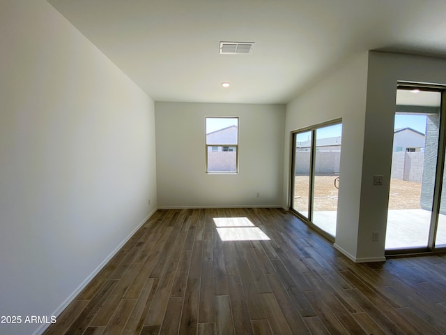 empty room featuring dark wood-type flooring, visible vents, and baseboards