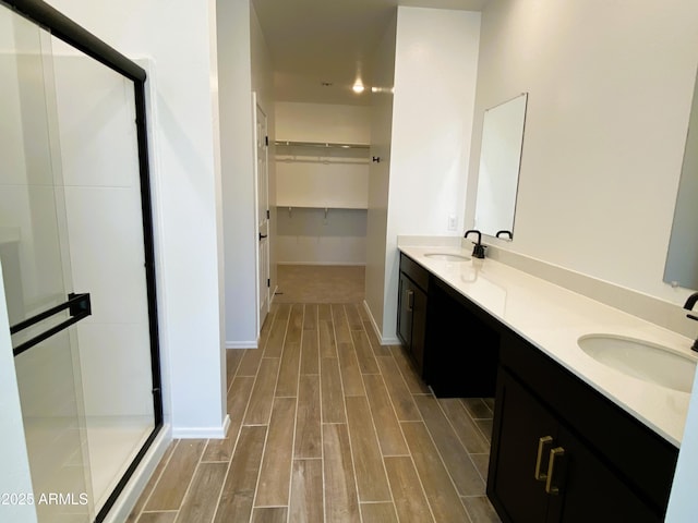 bathroom featuring a shower stall, double vanity, a sink, and wood tiled floor