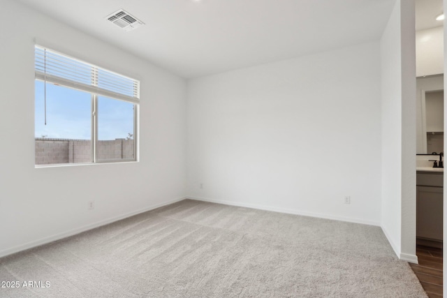 carpeted empty room with visible vents, baseboards, and a sink