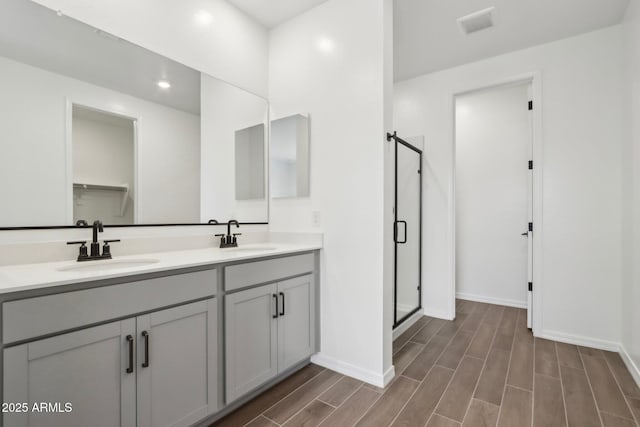 full bath with a sink, a shower stall, double vanity, and wood tiled floor
