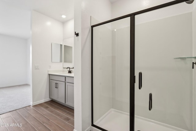 full bath with a shower stall, vanity, baseboards, and wood finish floors